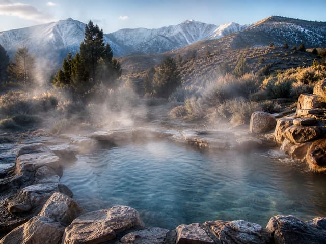 Editorial image of a rustic mountain hot spring pool with soft steam