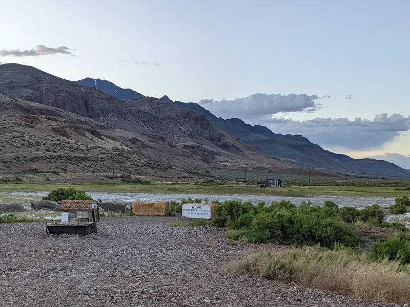 Gravel foreground with rustic signs and Steens Mountain behind Alvord Hot Springs; a historical property view