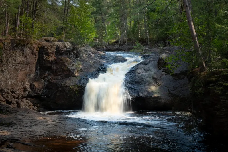 Waterfall flowing between dark rock ledges in the forest at Amnicon Falls State Park