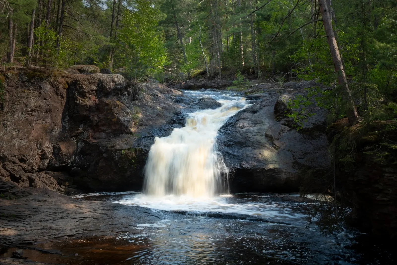 Waterfall flowing between dark rock ledges in the forest at Amnicon Falls State Park