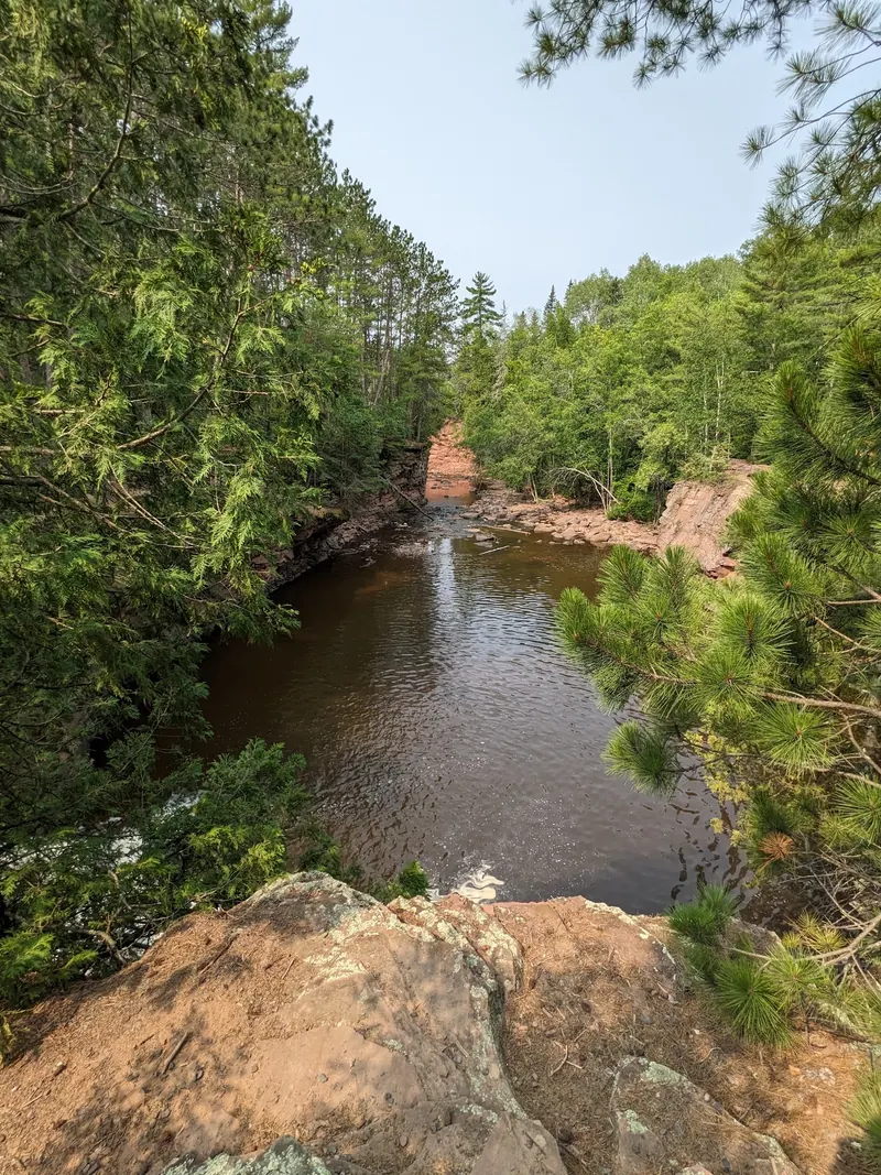 Amnicon River bordered by reddish rock banks and dense woodland