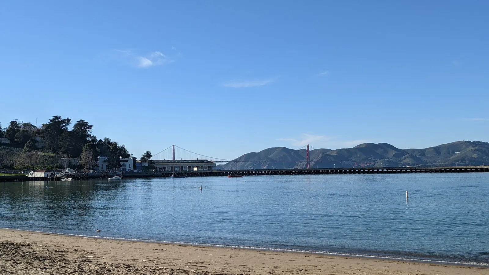 Sandy beach and bay water at Aquatic Park Cove with the Golden Gate Bridge in the distance