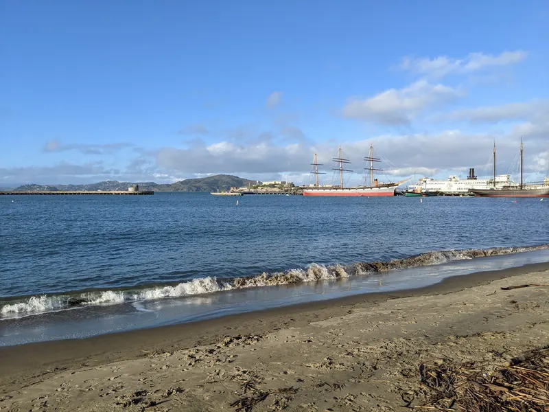 Past view of Aquatic Park's sandy shoreline with historic ships across the cove, not the current pier arrangement