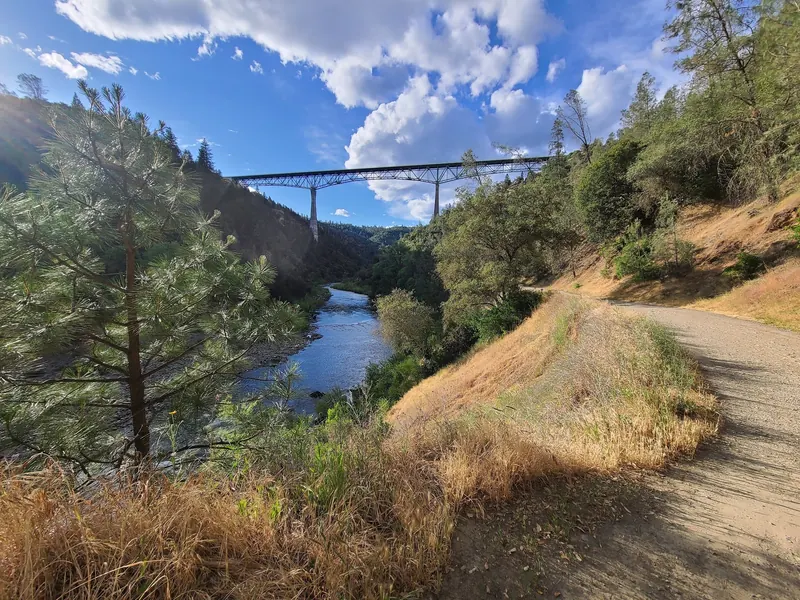 A canyon path beside the American River with Foresthill Bridge above