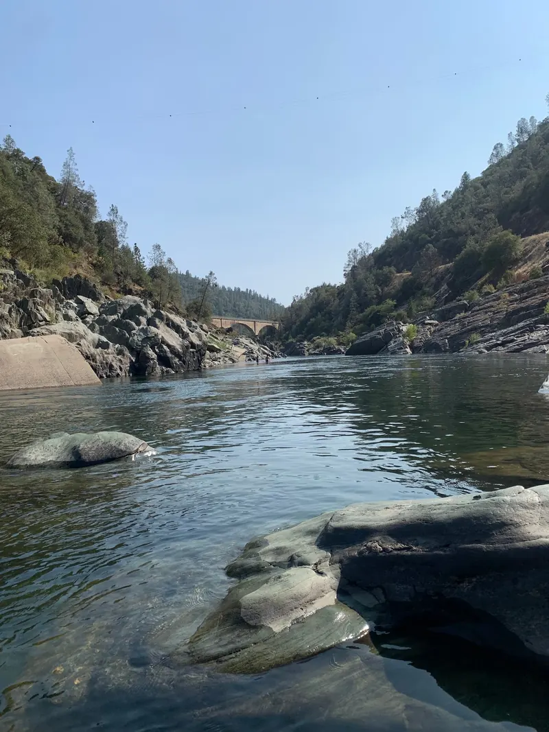 Historical American River corridor view with exposed rock banks and an arched bridge in the Auburn collection; not a recommended swimming entry