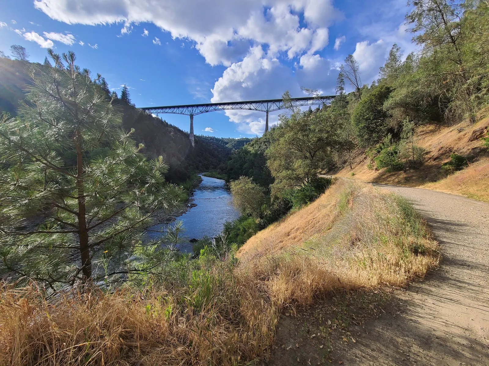 A canyon path beside the American River with Foresthill Bridge above