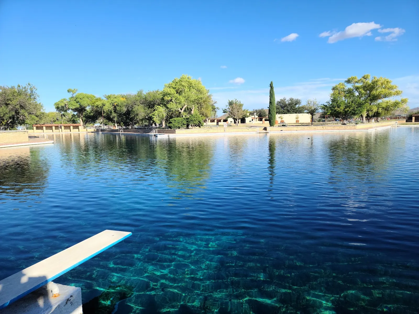 Balmorhea State Park swimming pool with a diving board, stone edges and trees across the water