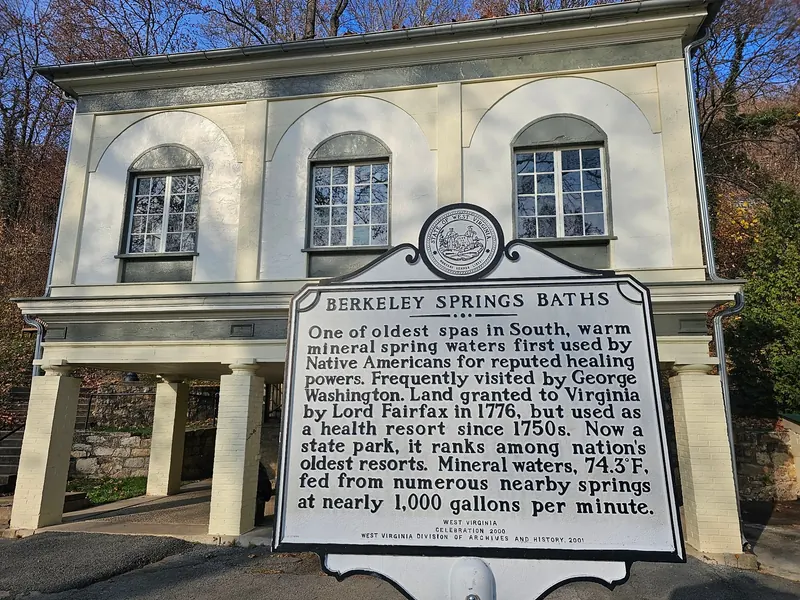 Berkeley Springs Baths historical marker in front of a pale yellow park building