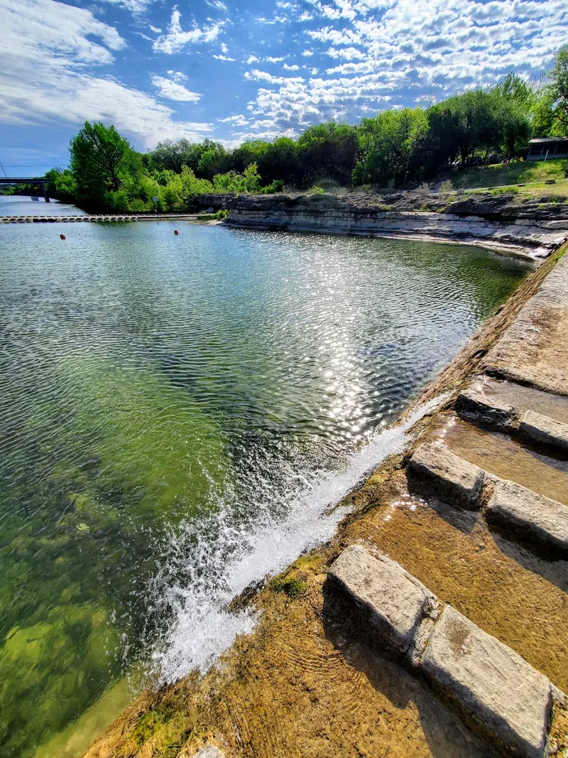 Water flowing over a low dam beside the rocky riverbank at Blanco State Park, Texas