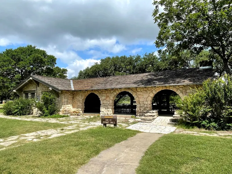 Stone picnic pavilion with arched openings and a permit-use sign at Blanco State Park