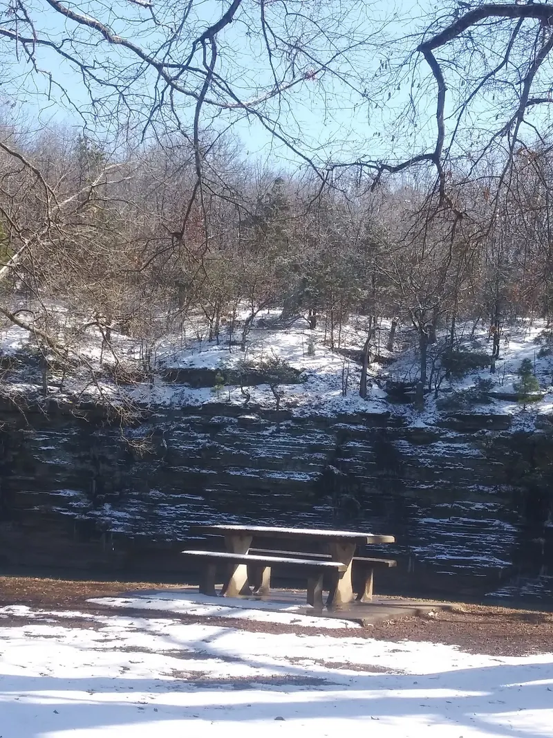 Picnic table beside the Mulberry River at Bluff Hole Park with snow on the opposite bluff; winter park context, not swimming conditions