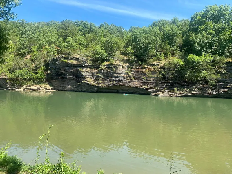 Sunlit layered bluff and green river water in the Bluff Hole Park collection, with a distant visitor; historical scenery, not an entry guide