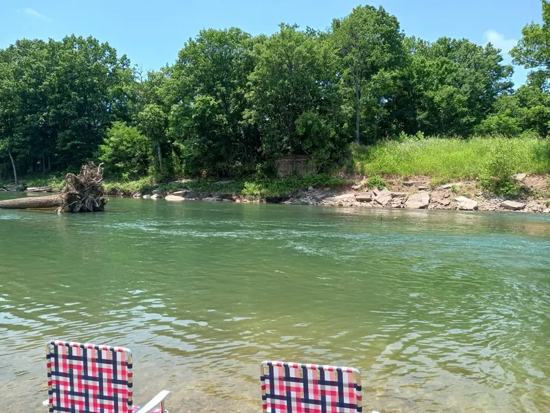 Creek water, a fallen tree and an opposite rock bank with two empty chairs in the foreground