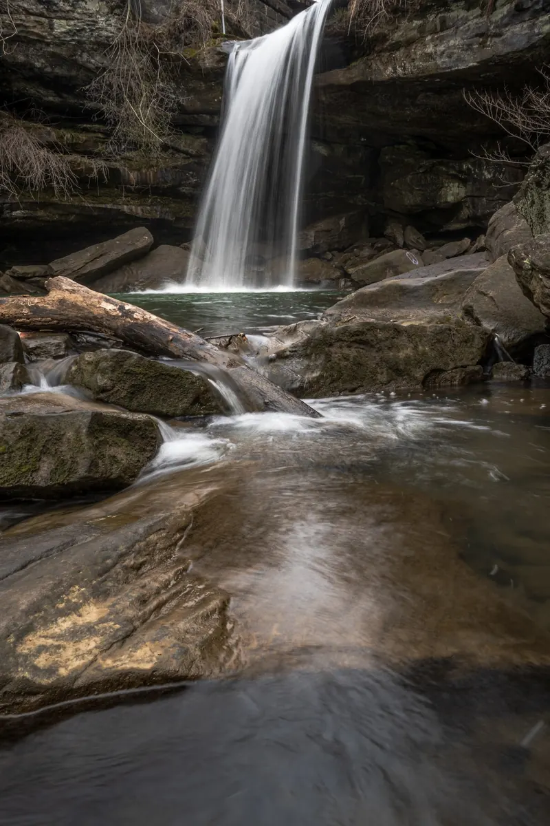 Long-exposure waterfall and rocky outflow beneath leafless branches in the Homewood Buttermilk Falls collection