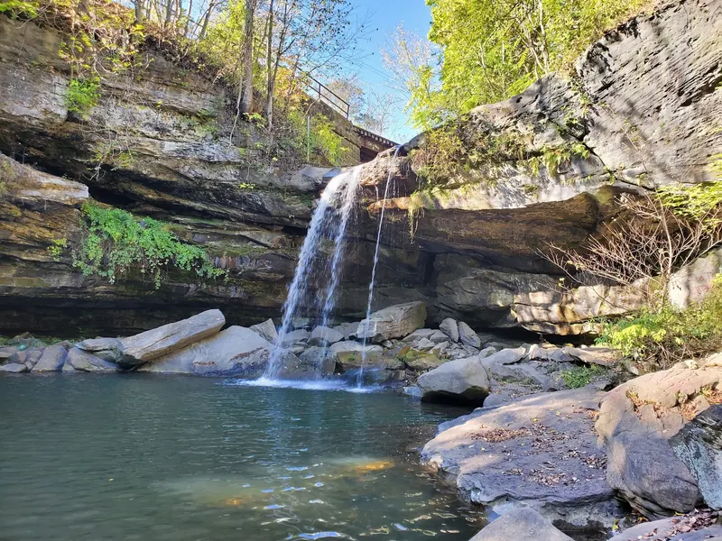 Buttermilk Falls dropping over layered sandstone into a pool among boulders and leafy trees in Homewood Borough