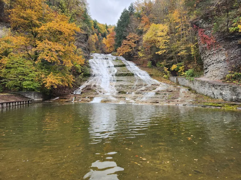 Main waterfall and lower pool at Buttermilk Falls State Park surrounded by autumn foliage