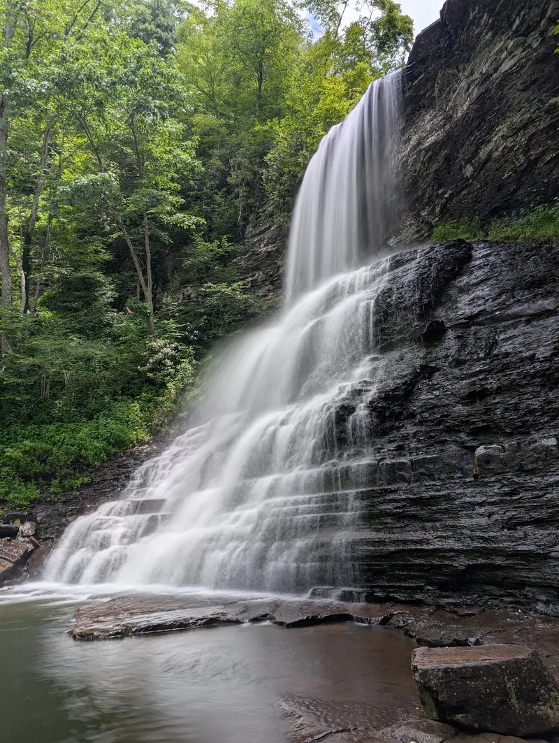 Cascade Falls pouring over layered rock into a pool below a wooded gorge wall
