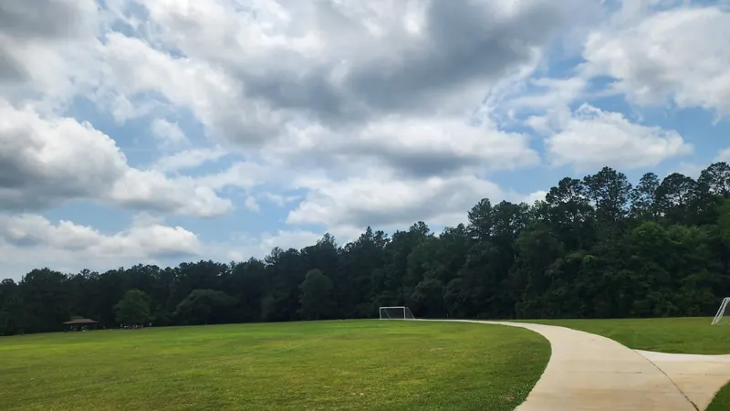Curved paved path beside an open playing field and pavilion at Chickasabogue Park
