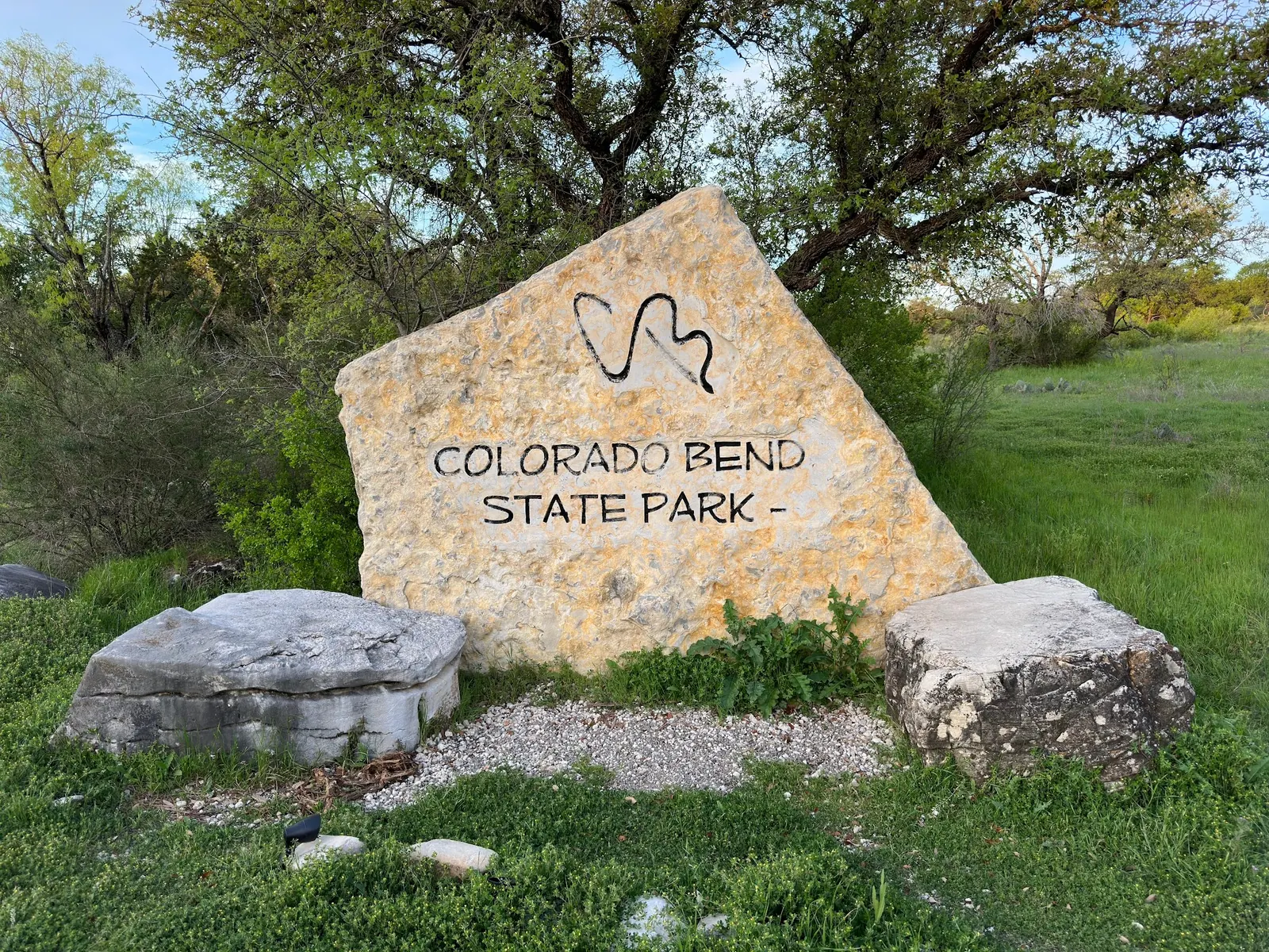 Colorado Bend State Park name carved into a stone sign beside grass and trees