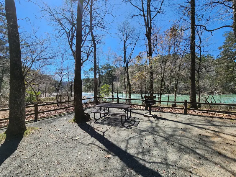 Picnic table and grill beside the river in Cossatot River State Park, behind a bank-restoration fence