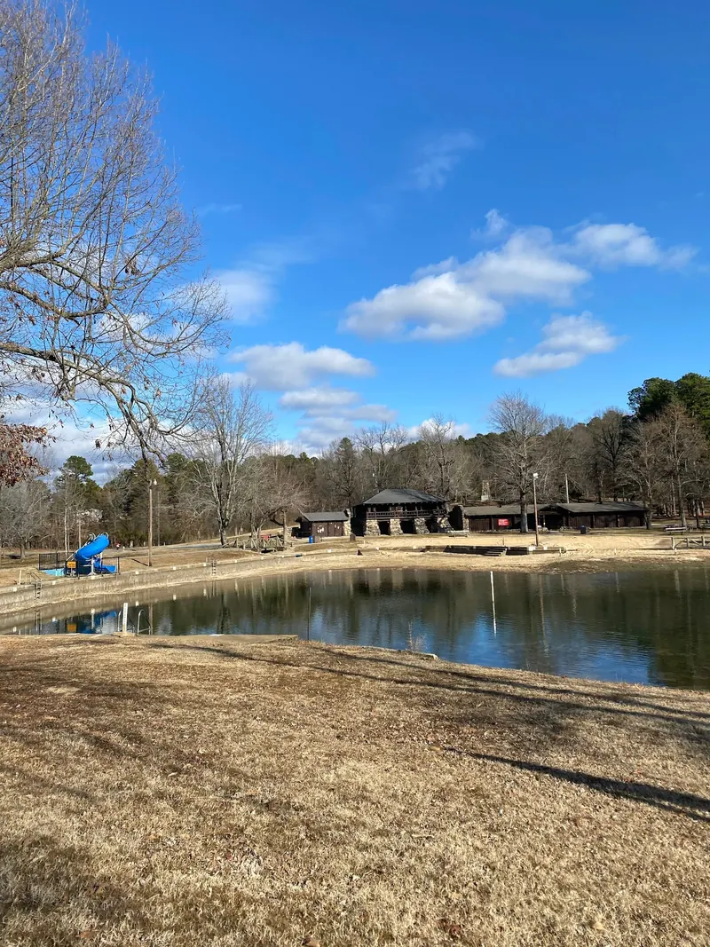 Lake shore with slide, swim-area steps and log-and-stone pavilion at Crowley's Ridge State Park; seasonal reference view, not current operating conditions