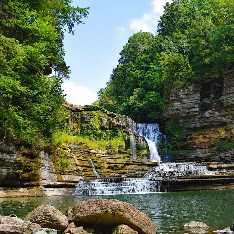 Cummins Falls cascading over layered rock ledges into a pool beneath wooded gorge walls