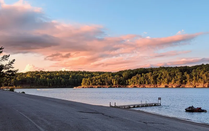 Sloping shore, low dock and personal watercraft beneath a pink evening sky in the Dam Site collection; historical lake context, not verified swim-area boundaries