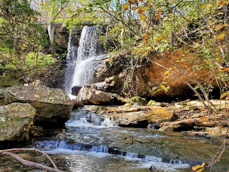 Woodland waterfall beneath a wooden footbridge with rocky creek ledges in the DeSoto park collection