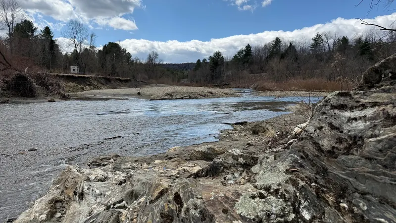 Dog River flowing around a gravel bar with bare trees and bedrock in the foreground