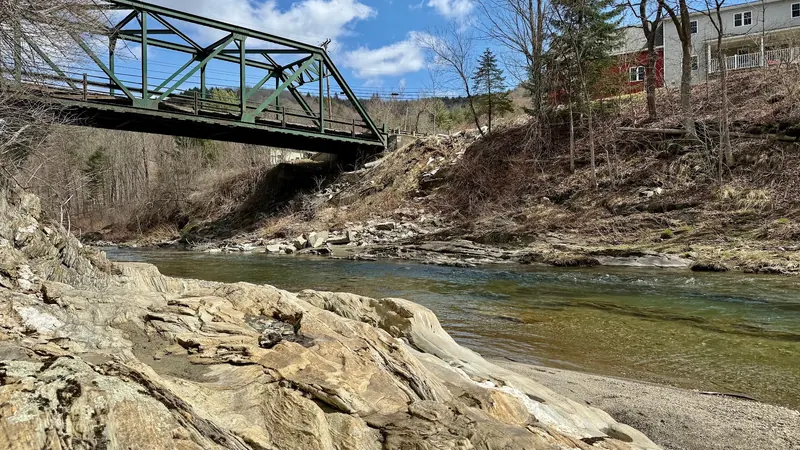 Green truss bridge spanning the Dog River above exposed bedrock in the natural-area collection