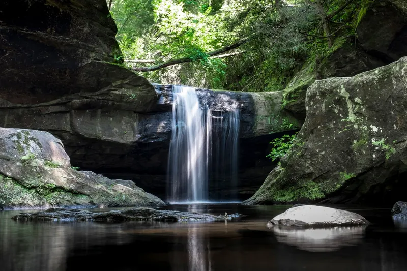 Dog Slaughter Falls cascading over a rock ledge into a pool surrounded by forest and moss-covered boulders