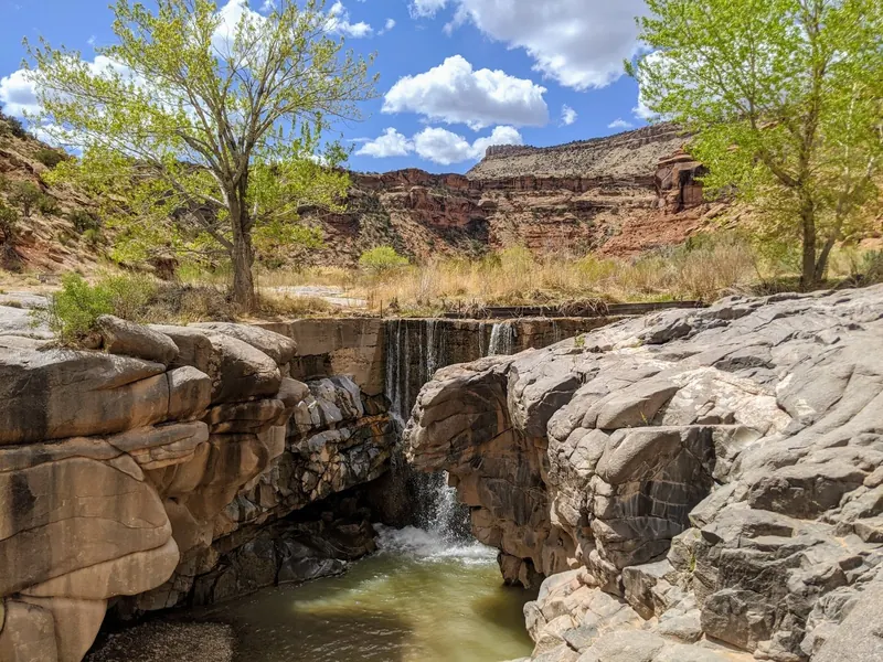 Small cascade over a concrete structure between rocks and trees in the Dominguez Canyon area