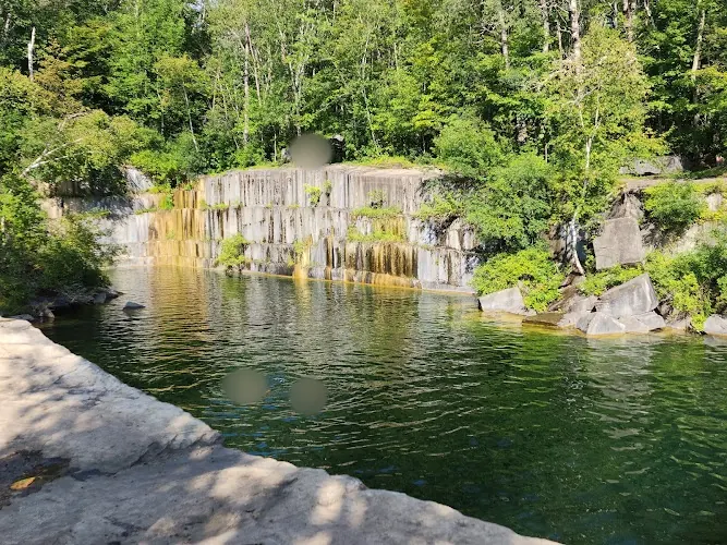 Marble quarry walls and wooded bank above the dark green water at Dorset Quarry; historical visitors blurred