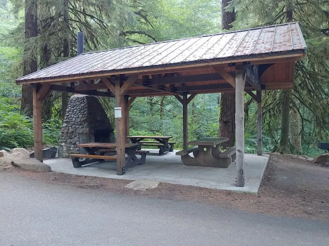 Open-sided timber picnic shelter with tables and a stone fireplace in the Dovre collection; historical facility view