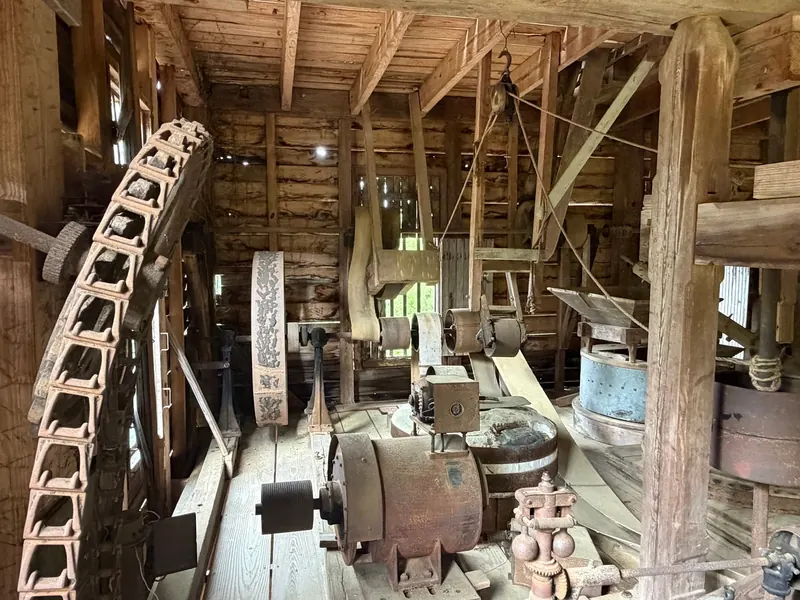 Historical wooden grist mill interior with stone grinding equipment and belt-driven machinery at Dunn's Falls; not confirmation of current interior access