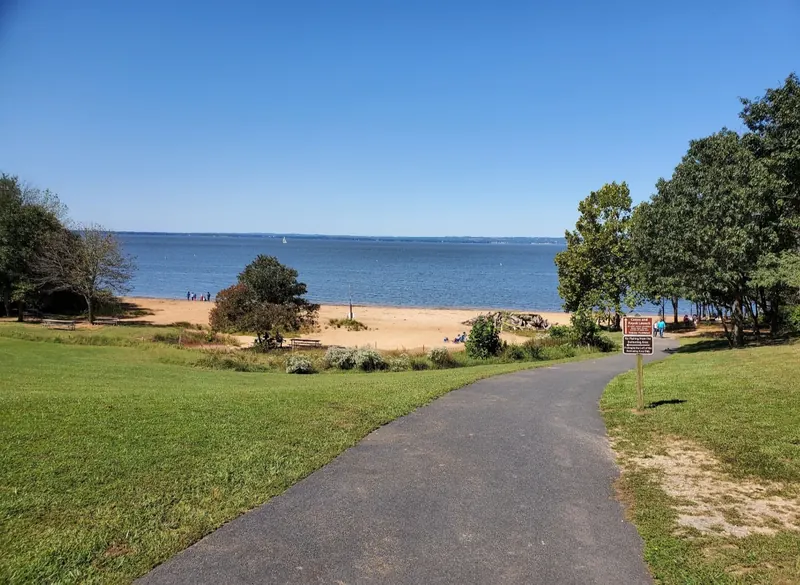 Paved path descending toward North East Beach at Elk Neck State Park, with sand, picnic tables and bay views