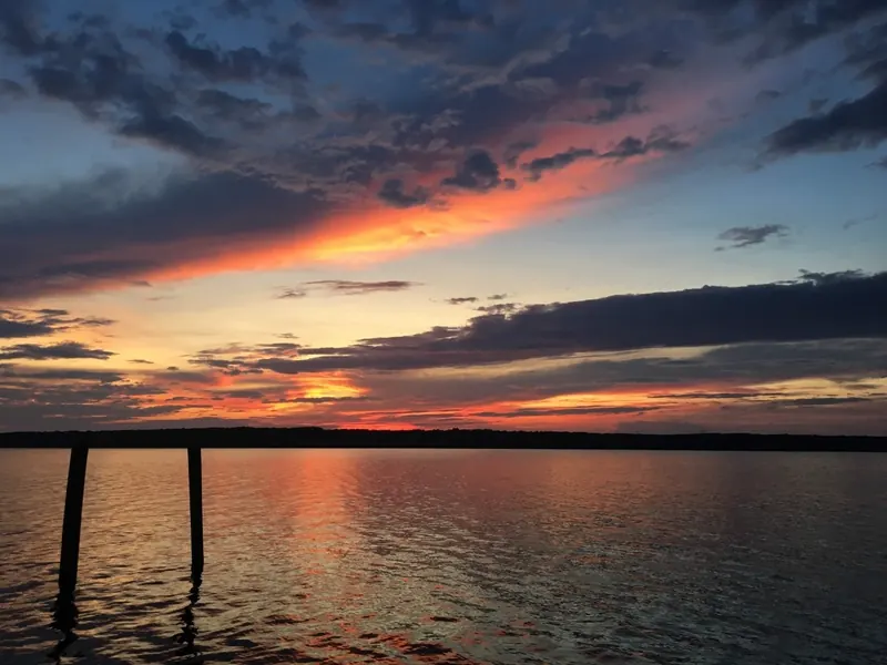 Orange sunset clouds reflected across Falls Lake with wooden posts in the foreground