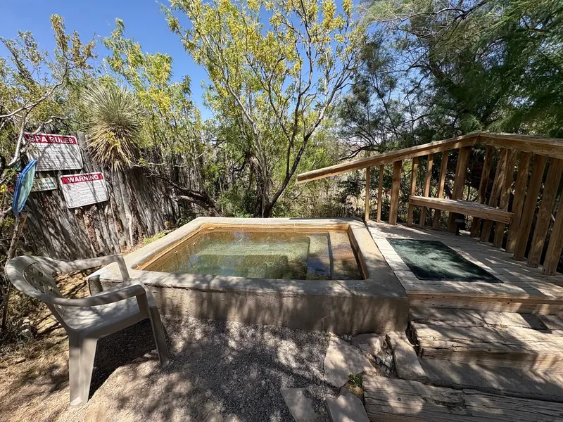 Small rectangular soaking tub beside a wooden deck and warning signs in the Faywood Hot Springs collection; historical layout, not current temperature or accessibility evidence