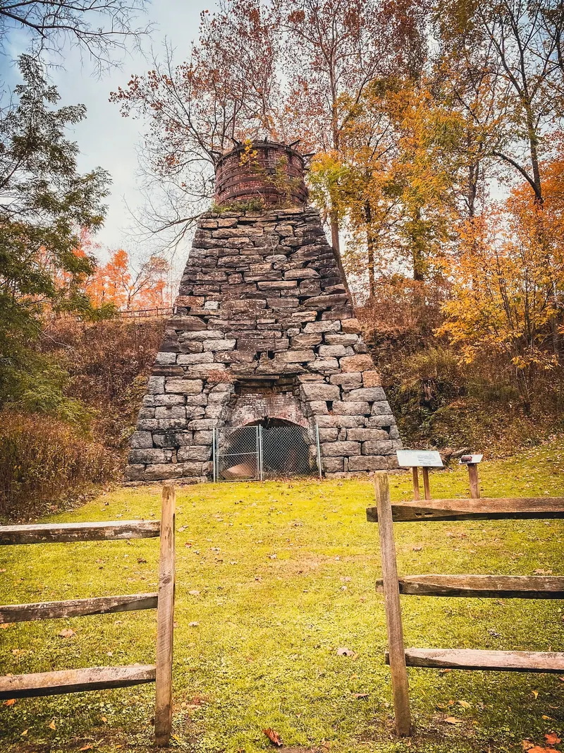 Historic iron furnace at Foster Falls behind a wooden fence, surrounded by autumn trees