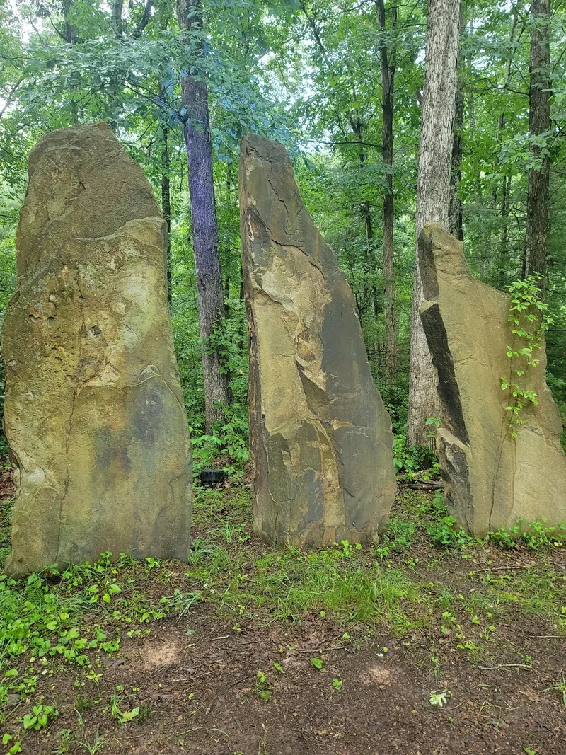 Three upright standing stones among leafy trees at Four Quarters Interfaith Sanctuary