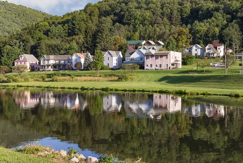 Galeton houses reflected across Berger Lake beside a grassy shoreline