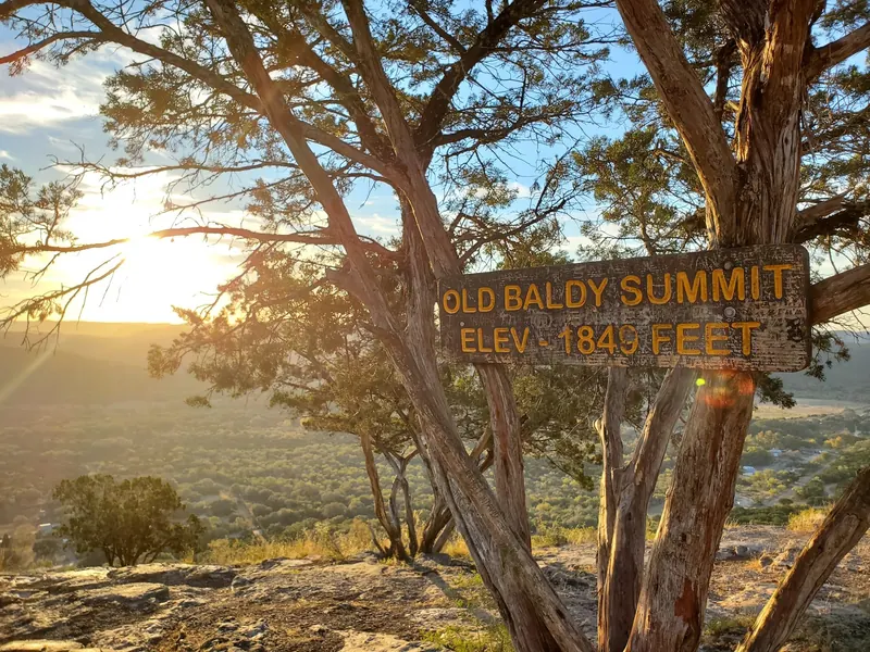 Old Baldy summit sign among trees with sunset light over the valley