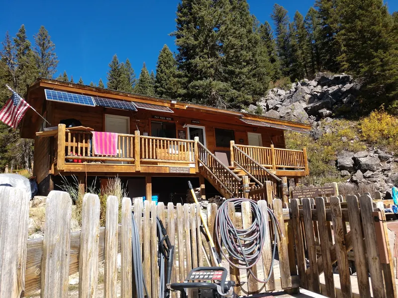 Wooden visitor building and fee window at Granite Hot Springs beneath a forested rock slope