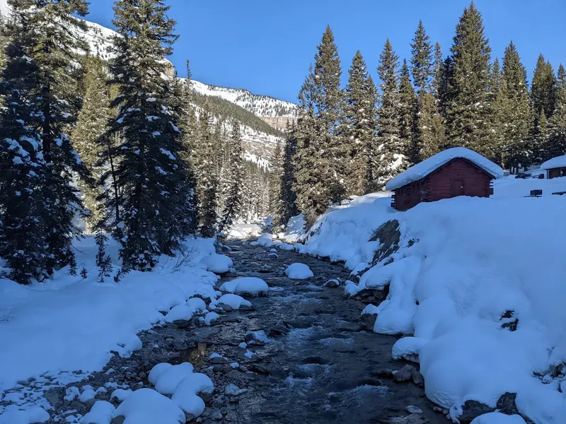 Snow-covered banks and a red cabin beside Granite Creek near the hot springs; winter scenery, not a swimming entry