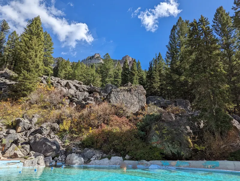Granite Hot Springs soaking pool below a rocky, forested slope; visitors' faces blurred for privacy