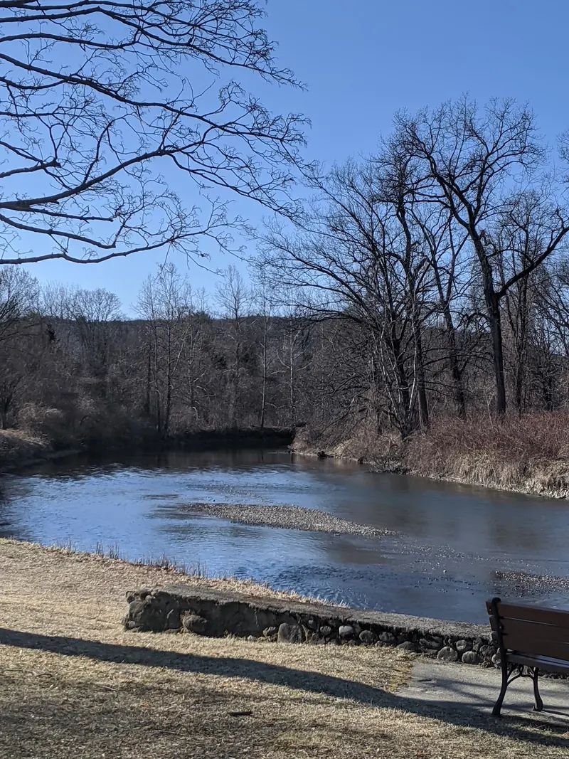 Riverside bench and stone wall beside the Green River with leafless trees, showing a past off-season visit
