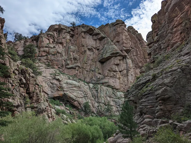 Tall fractured rock walls and shrubs in Guffey Gorge beneath a partly cloudy sky