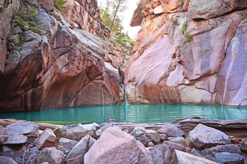 Cascade and creek pool between pink rock walls at Guffey Gorge, with fallen wood along the rocky shore