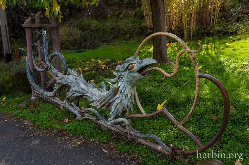 Operator-watermarked decorative metal dragon gate beside a shaded garden path at Harbin Hot Springs; not a verified entrance