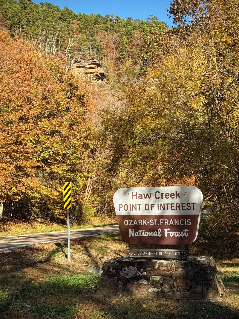Haw Creek Point of Interest sign identifying Ozark St Francis National Forest beside an autumn wooded road; historical arrival context